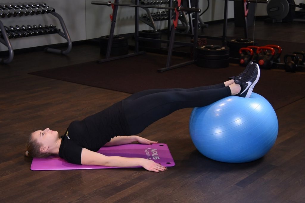 Wznosy bioder z prostymi nogami na piłce do ćwiczeń